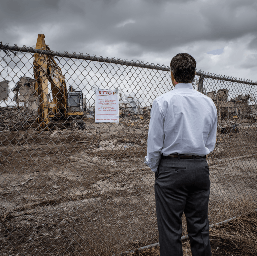 Developer looking through a fence at a stalled demolition site with a stop-work notice